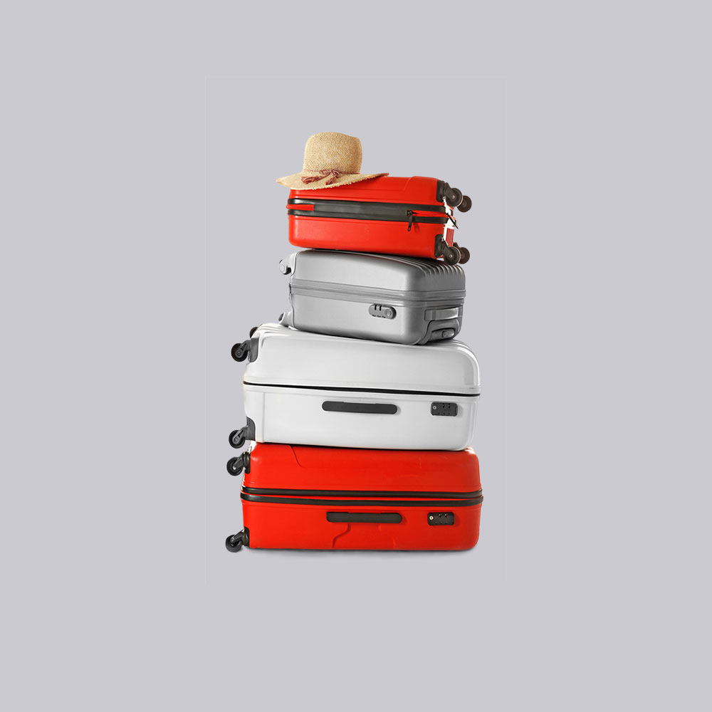 Family suitcases in red, silver and white stacked with a sun hat balanced on top