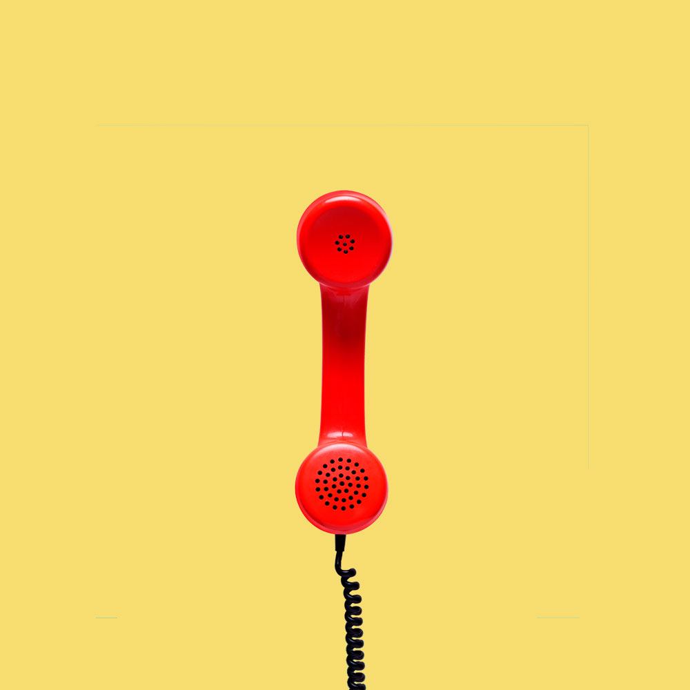 Red phone and black cable sitting on a yellow brackground